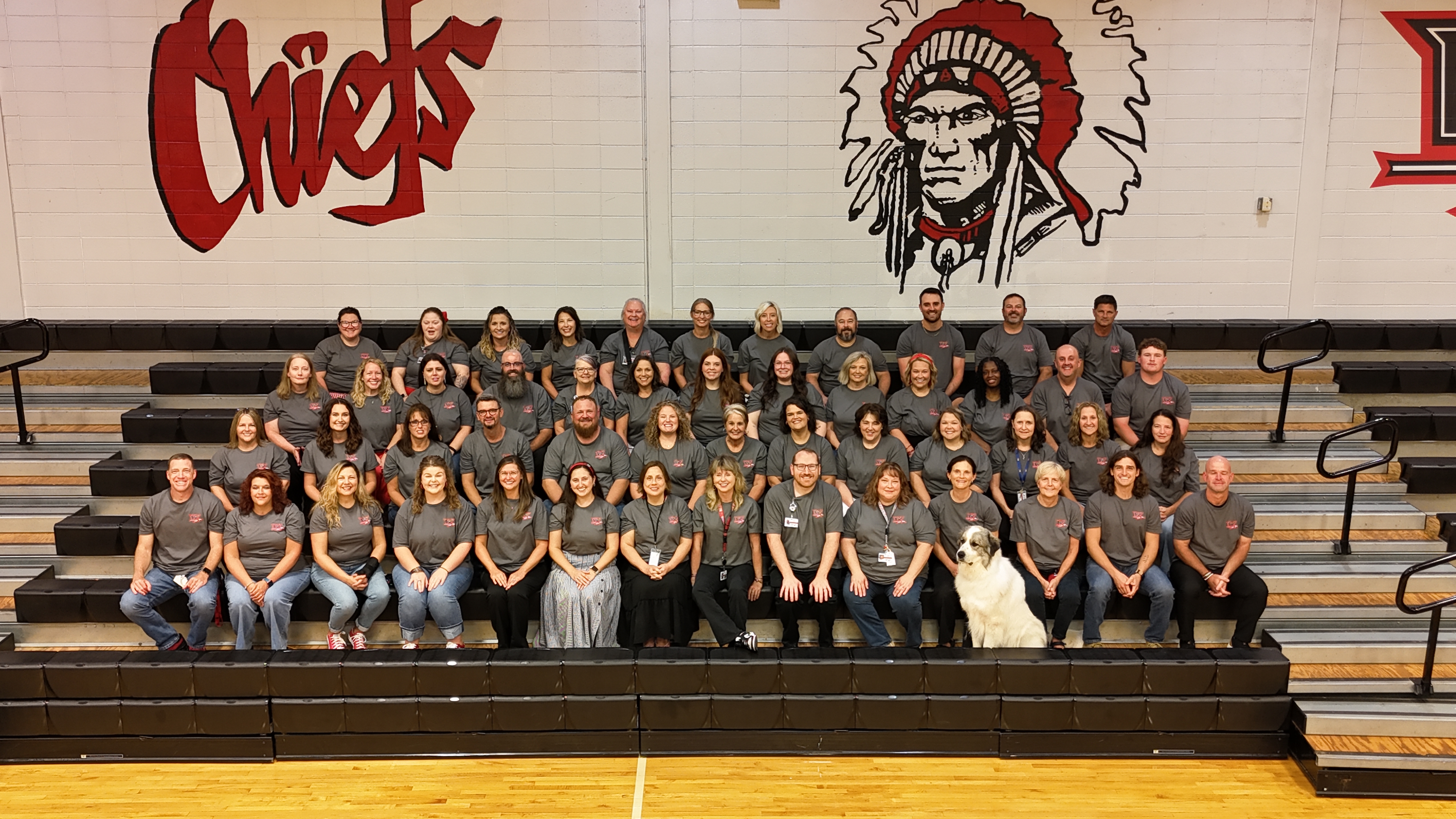 A group in gray shirts pose in a gym with "Chiefs" on the wall.