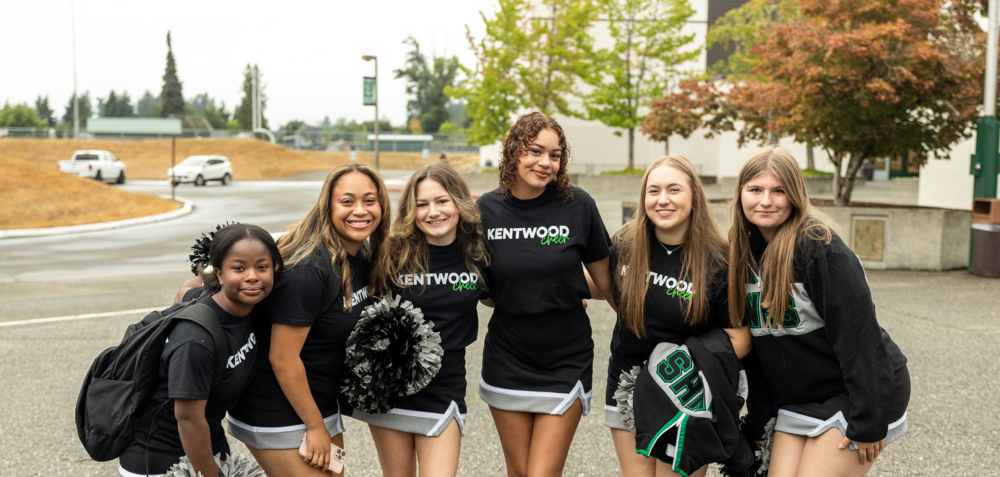 Cheerleaders in matching uniforms stand together outdoors, smiling. 