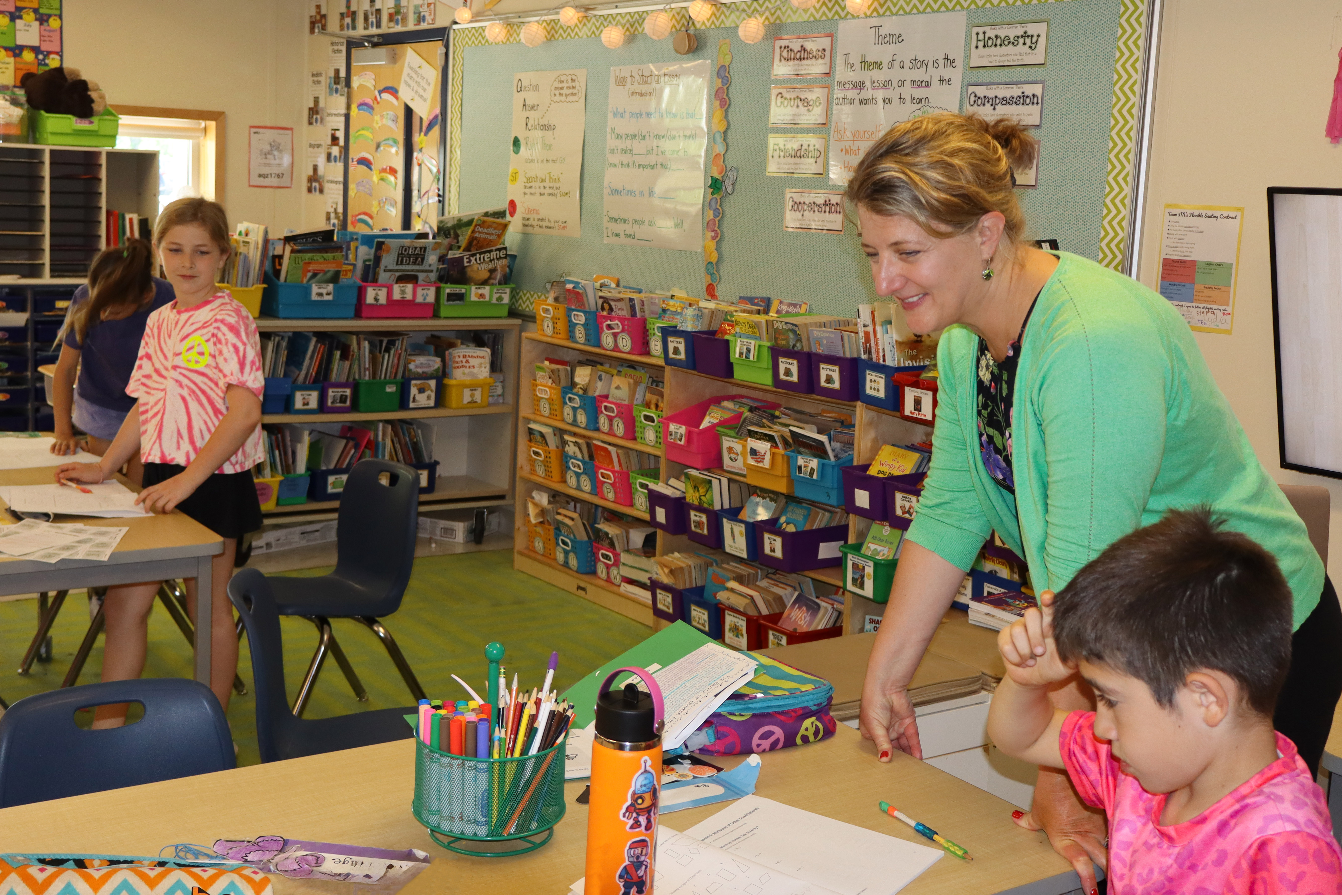 superintendent leaning over a desk with a student in the classroom with others standing around