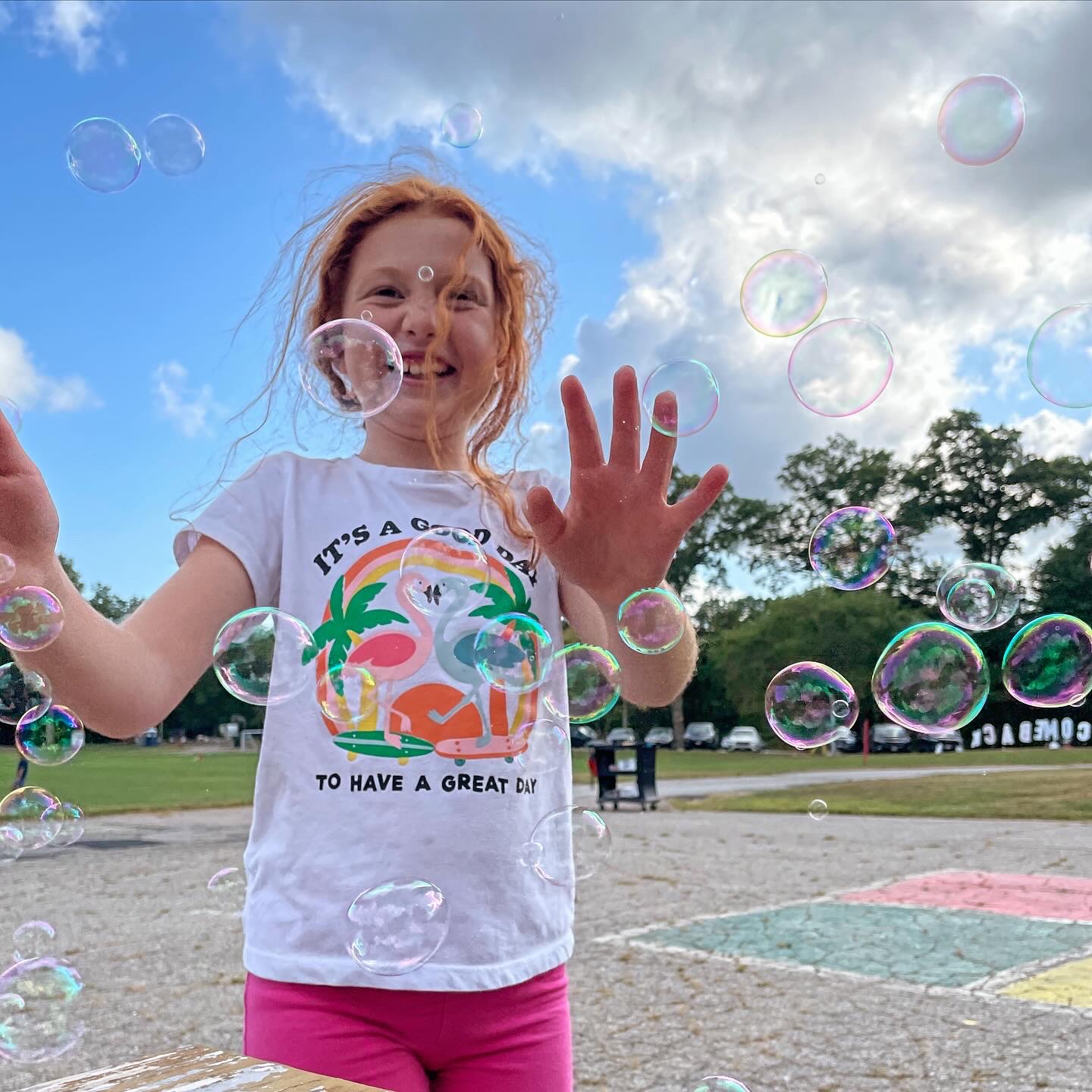 Smiling child with red hair has their arms in front of them while bubbles blow