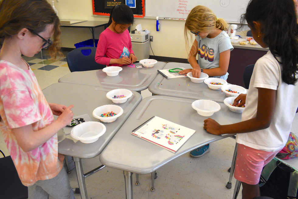 Children gathered around a table in a classroom setting, engaging with colorful craft supplies.