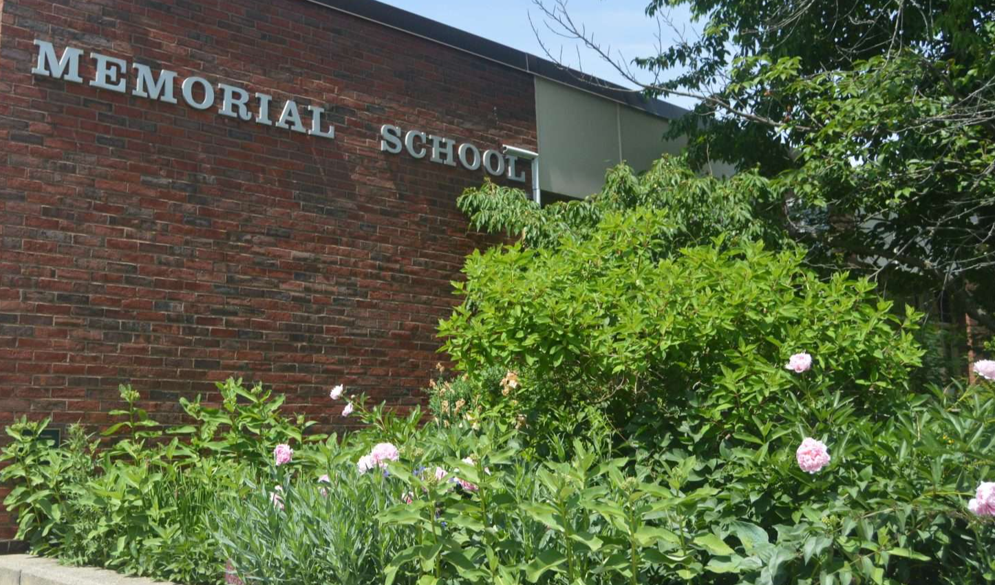 Memorial School Building With Sign Showing and Flowered Bushes in the Front