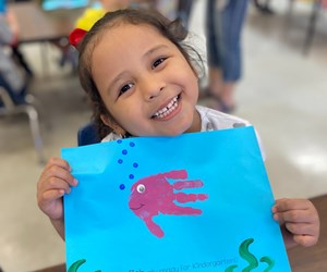 student smiling showing her artwork