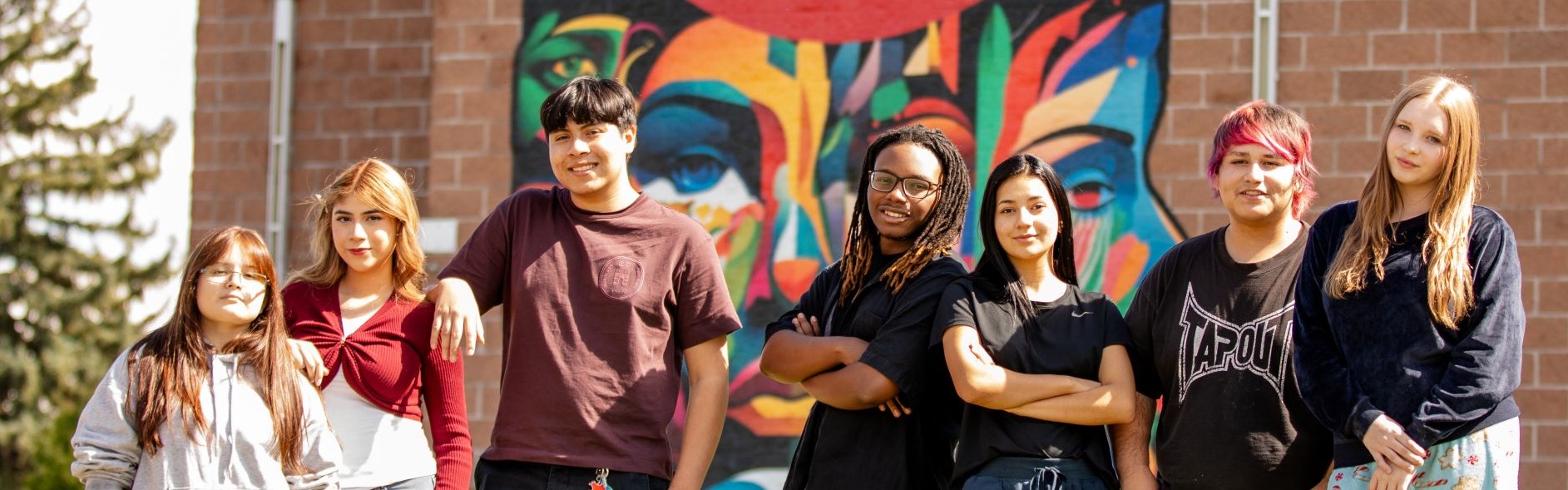 NEC students smile in front of a colorful mural