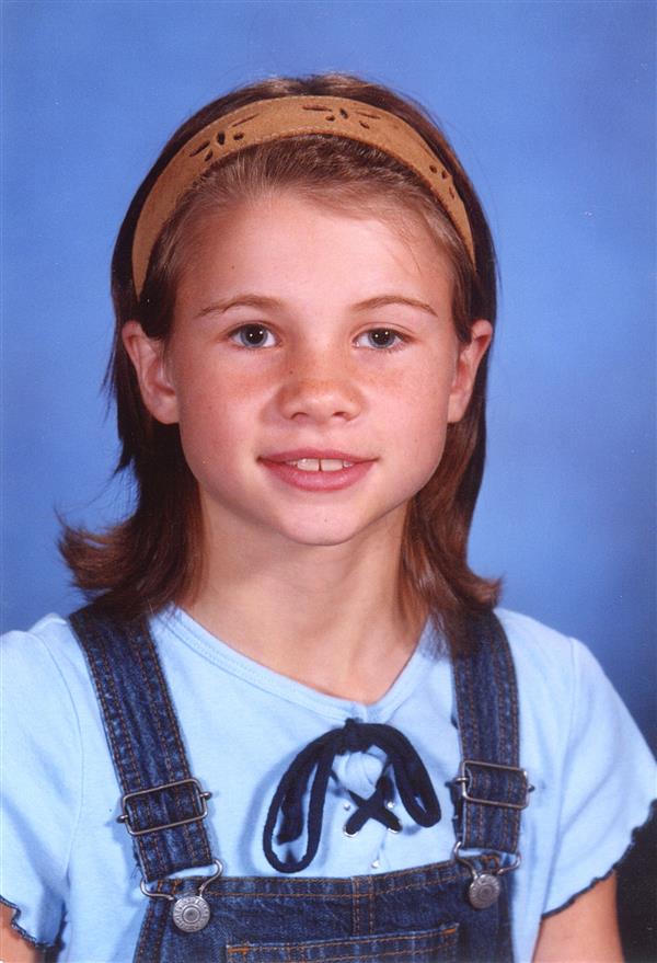 A girl wearing a green headband and a denim jumper with white shirt inside.