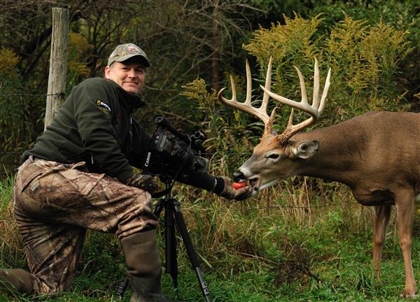 A hunter wearing full gear with his weapon while feeding a deer.