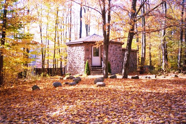 A stone building, possibly a cabin or small house, sits nestled amongst the trees in a forest.