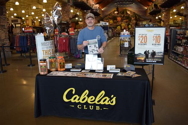 A man wearing a powder blue shirt standing with the signage of Cabelas