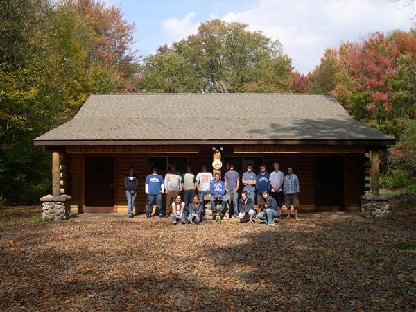 People posing for a picture in front of a cabin in the middle of a forest.