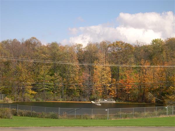 A lake surrounded by colorful trees in the fall. A fence runs along the edge of the water.