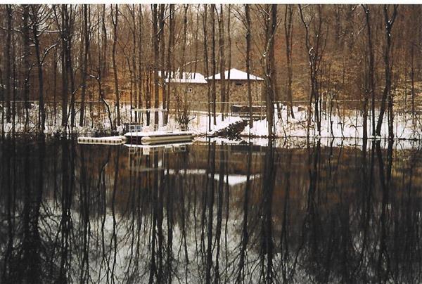 A wooden dock covered in snow juts out into a frozen lake. Snow-covered trees line the shore of the lake.