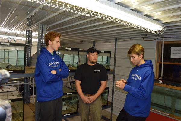 A guy wearing black shirt and a cap, and two boys wearing blue sweater.