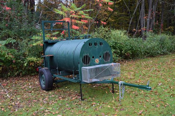 A green metal barrel with a lid sits on a grassy field.