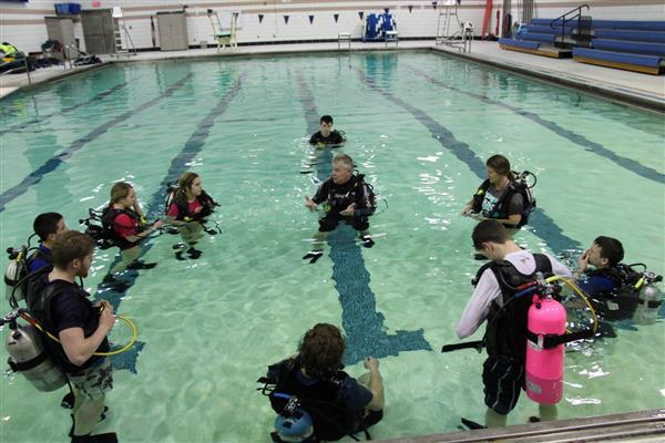 A guy coaching his students about SCUBA in the pool.