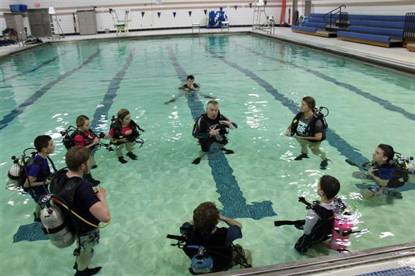 A guy coaching his students about SCUBA in the pool.