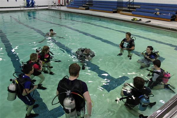 A guy coaching his students about SCUBA in the pool.