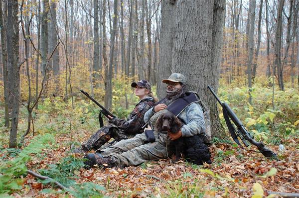 Two hunters wearing their full gear with their hunting gun together with their dog in the middle of a forest.