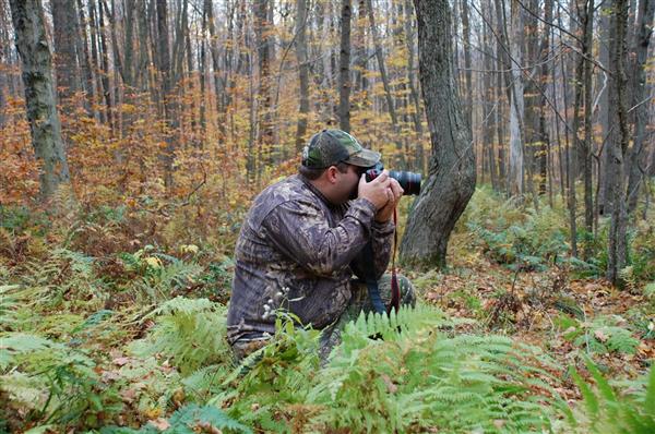 A hunter with his camera, taking pictures in the middle of a forest.