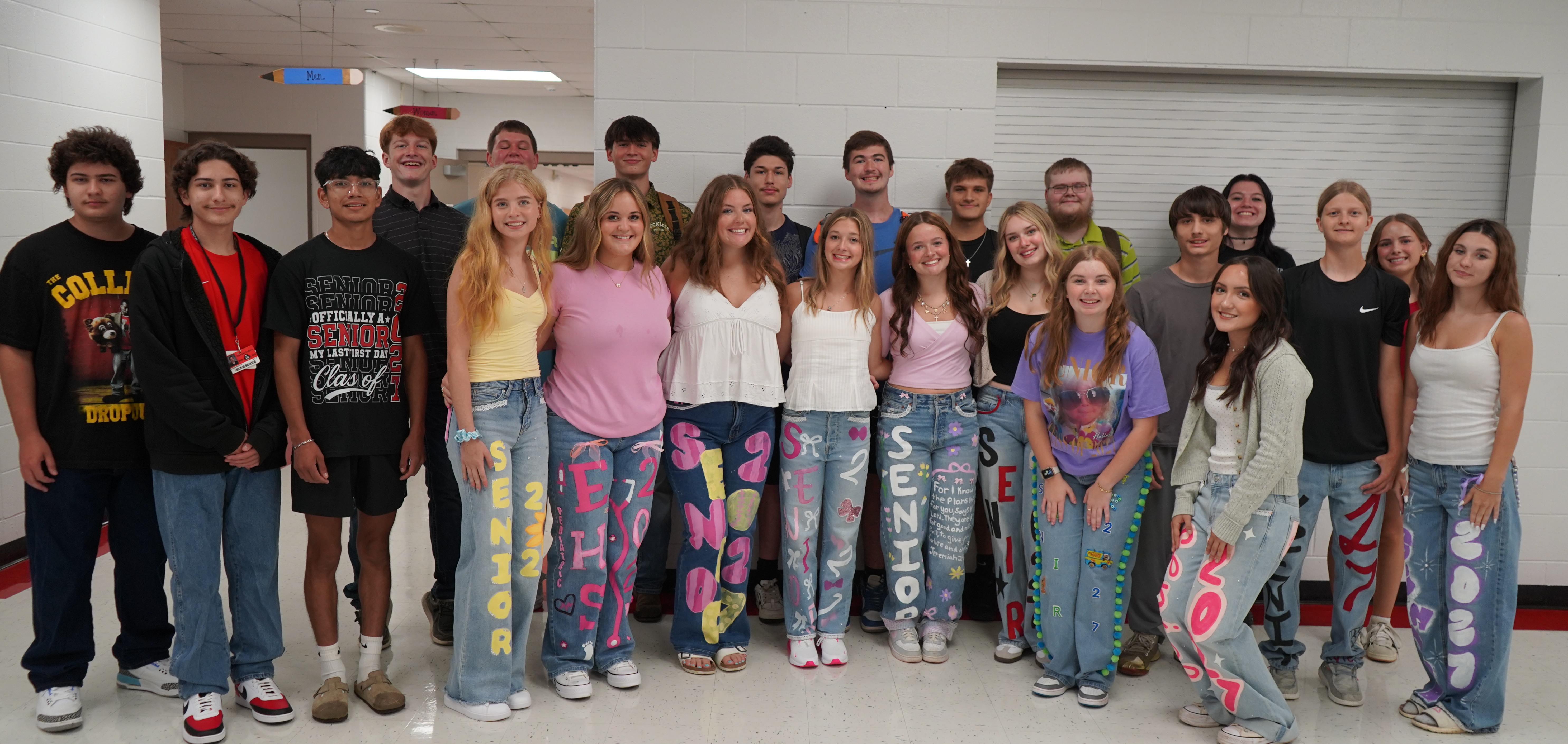 A group of people, both male and female, in various colored jeans and tops, pose together.