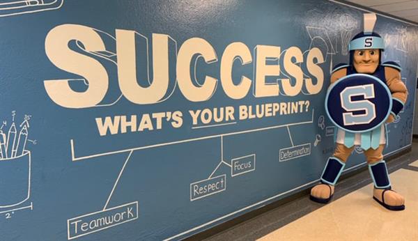 Spartan mascot in front of wall that says, "Success, what's your blueprint?"