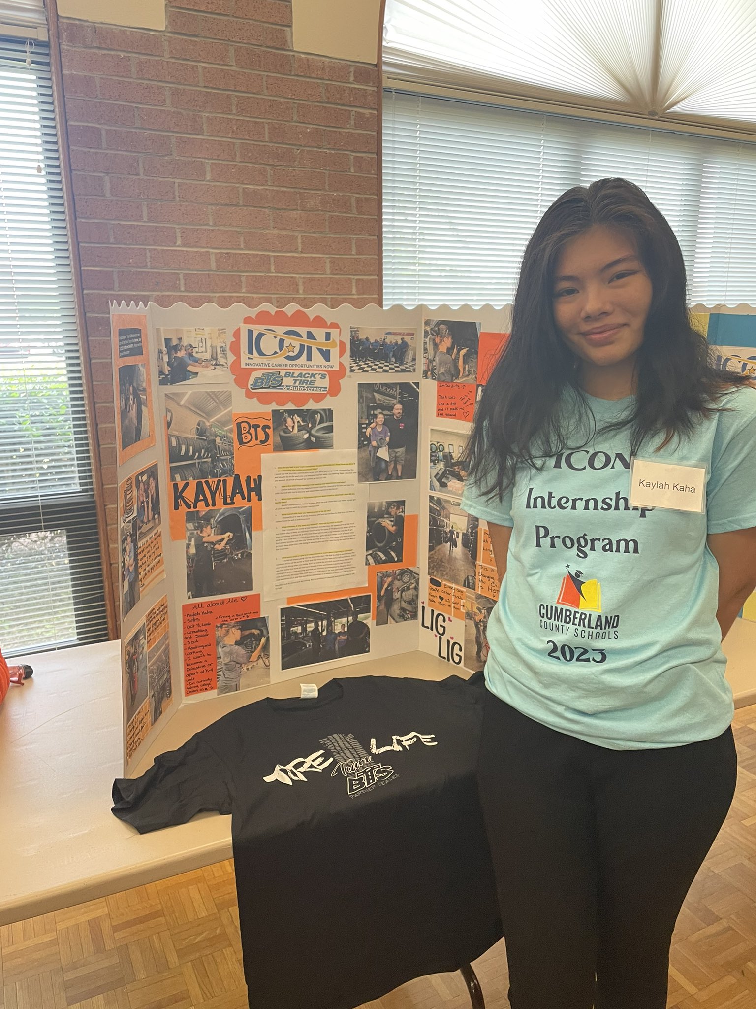 A female student posing in front of her summer internship poster board that she created.