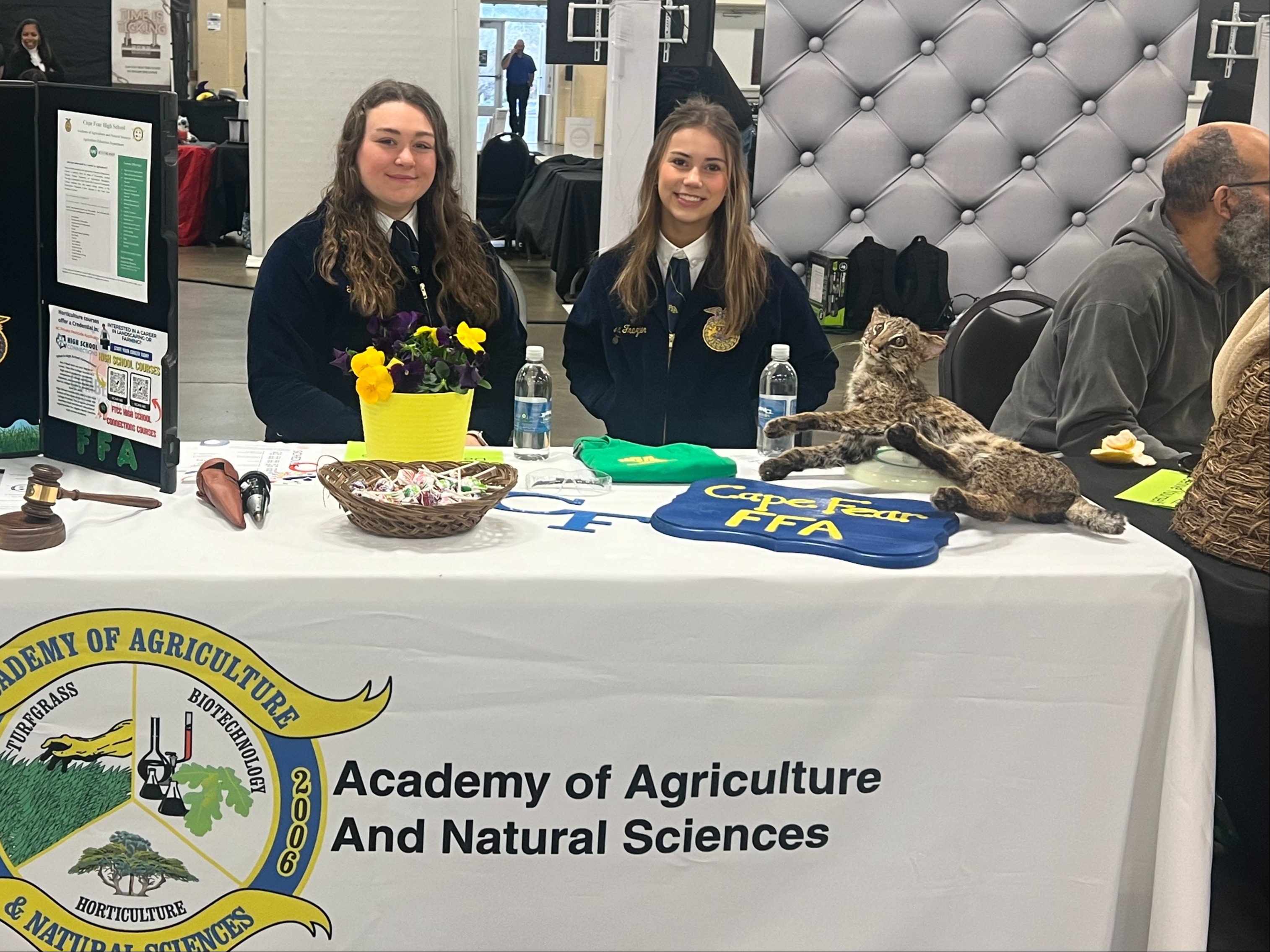 Two students sitting at the Academy of Agriculture and Natural Sciences Table set up at  an event posing for a photo.