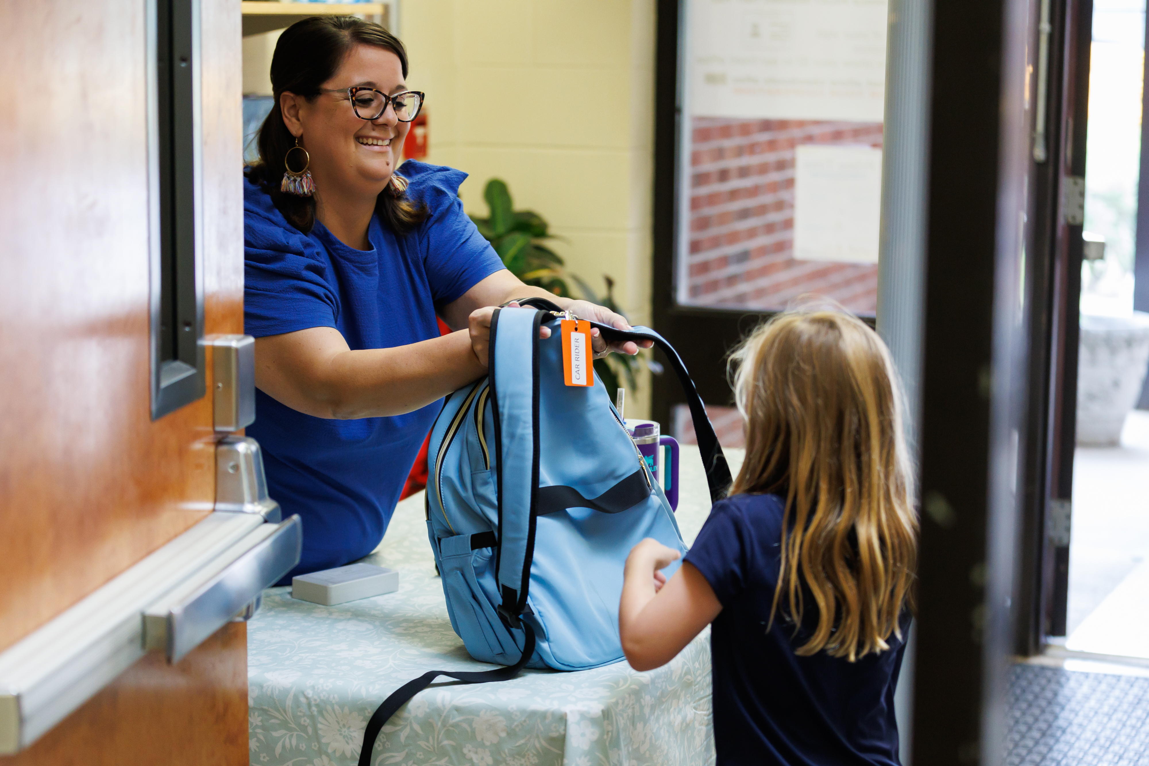 Principal handing a student her backpack with a smile.