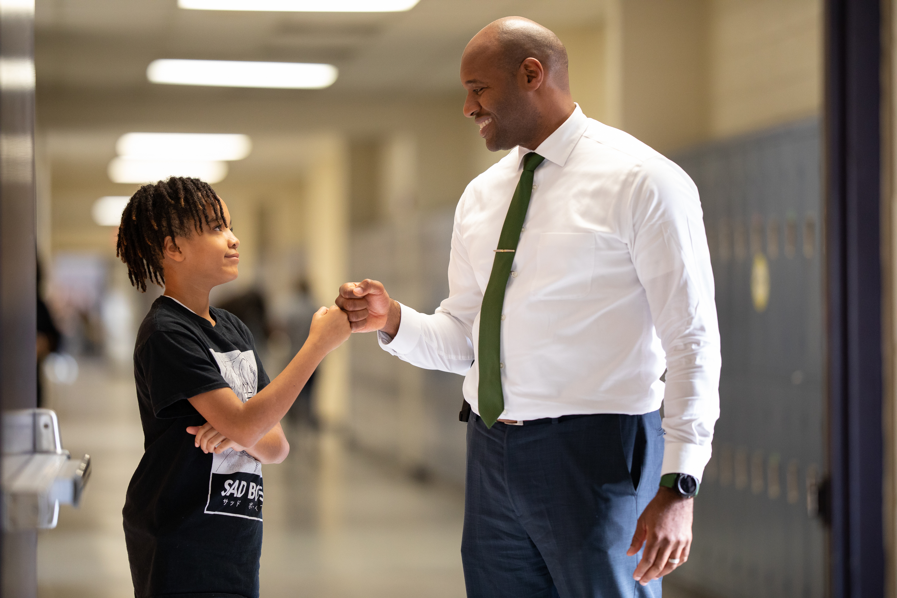 An adult and student share a fist bump in the hallway