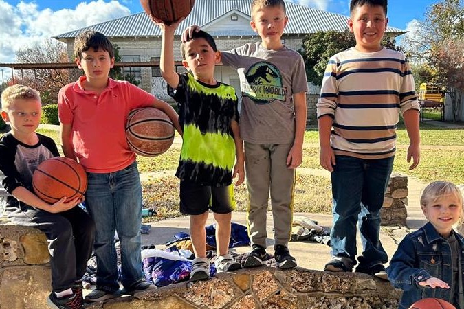 Six students standing on a rock wall with basketballs 