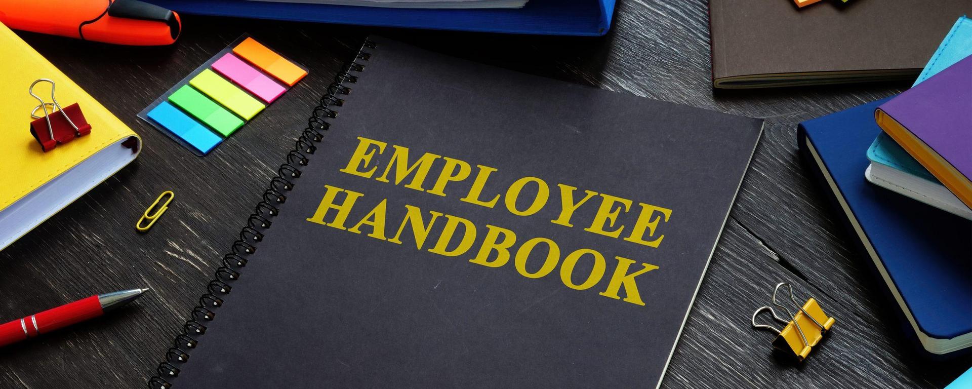 an image of school supplies on a desk, including a notebook that reads "employee handbook" on the cover