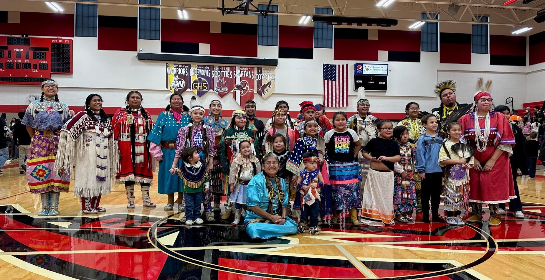students wearing tribal clothes gather for a group picture in a gym