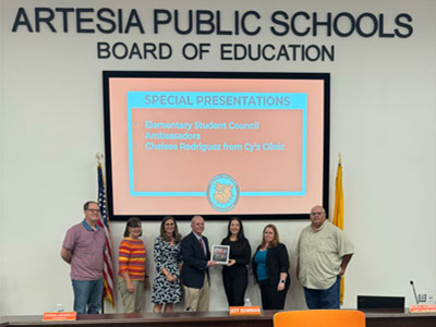 A photo of board members standing in front of a sign that says Artesia Public Schools Board of Education