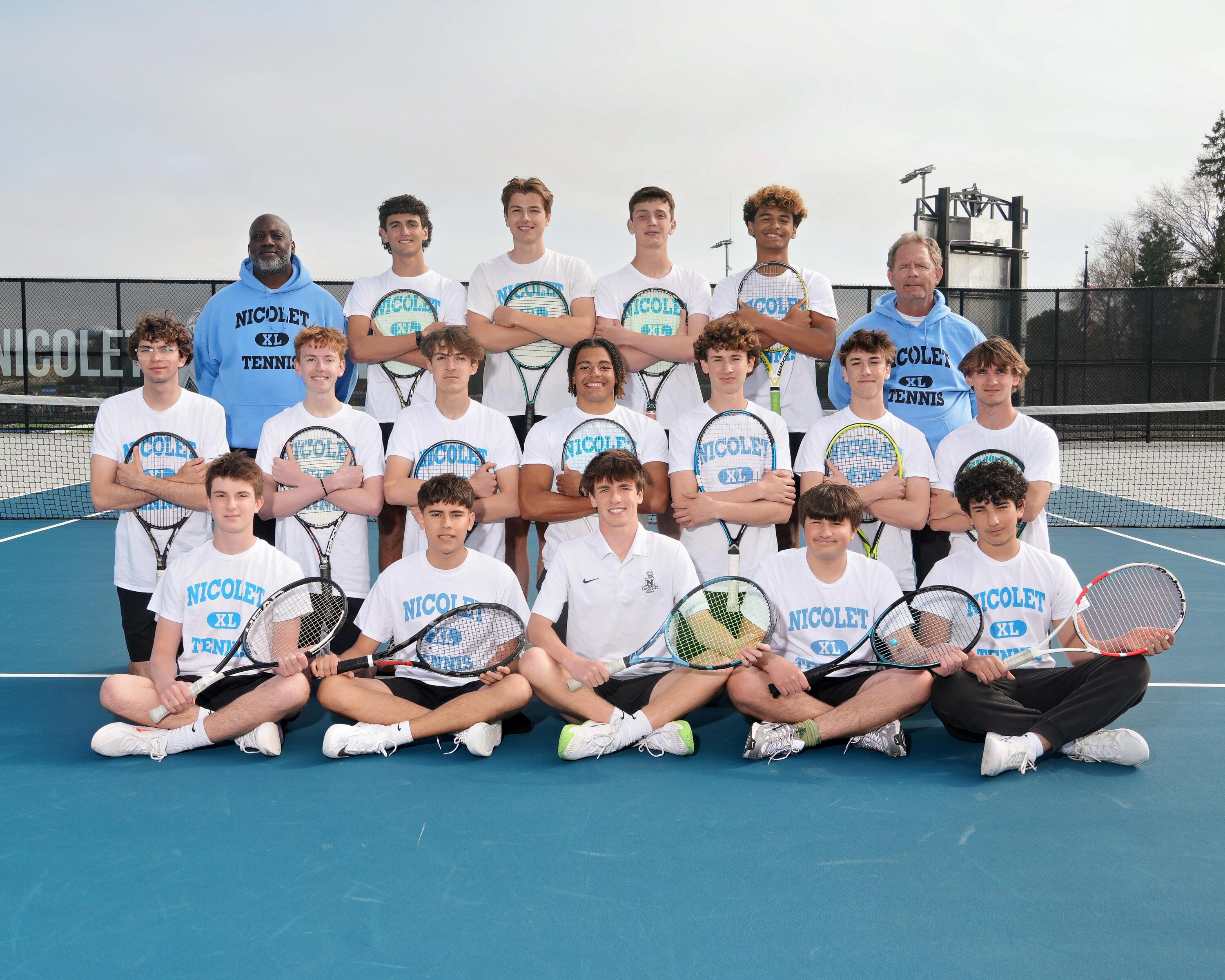 A group photo of a tennis team on a court, with players in white shirts and shorts holding rackets.