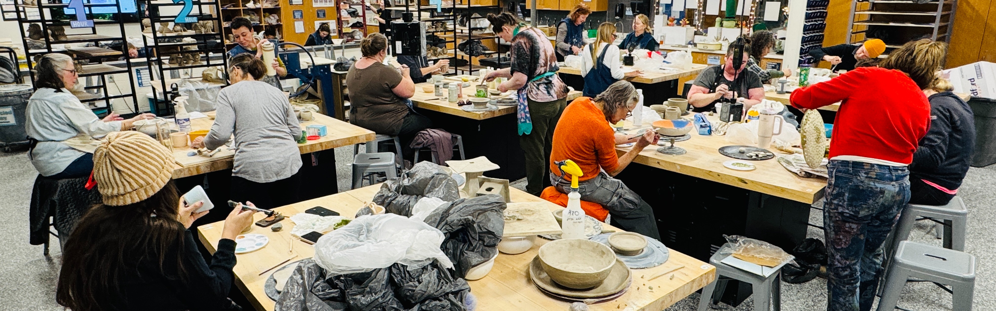 Several people work at tables in a room with wood paneling and white walls. Some wear hats.