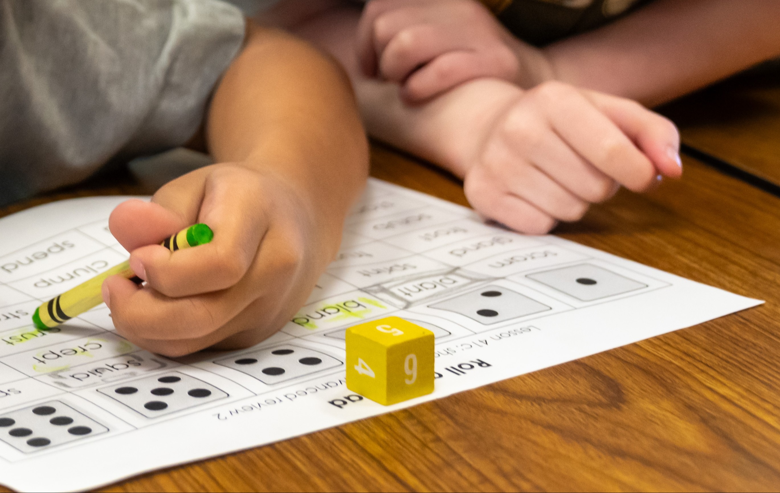 Child using a crayon to color in a number nine on a worksheet, with a small cube.