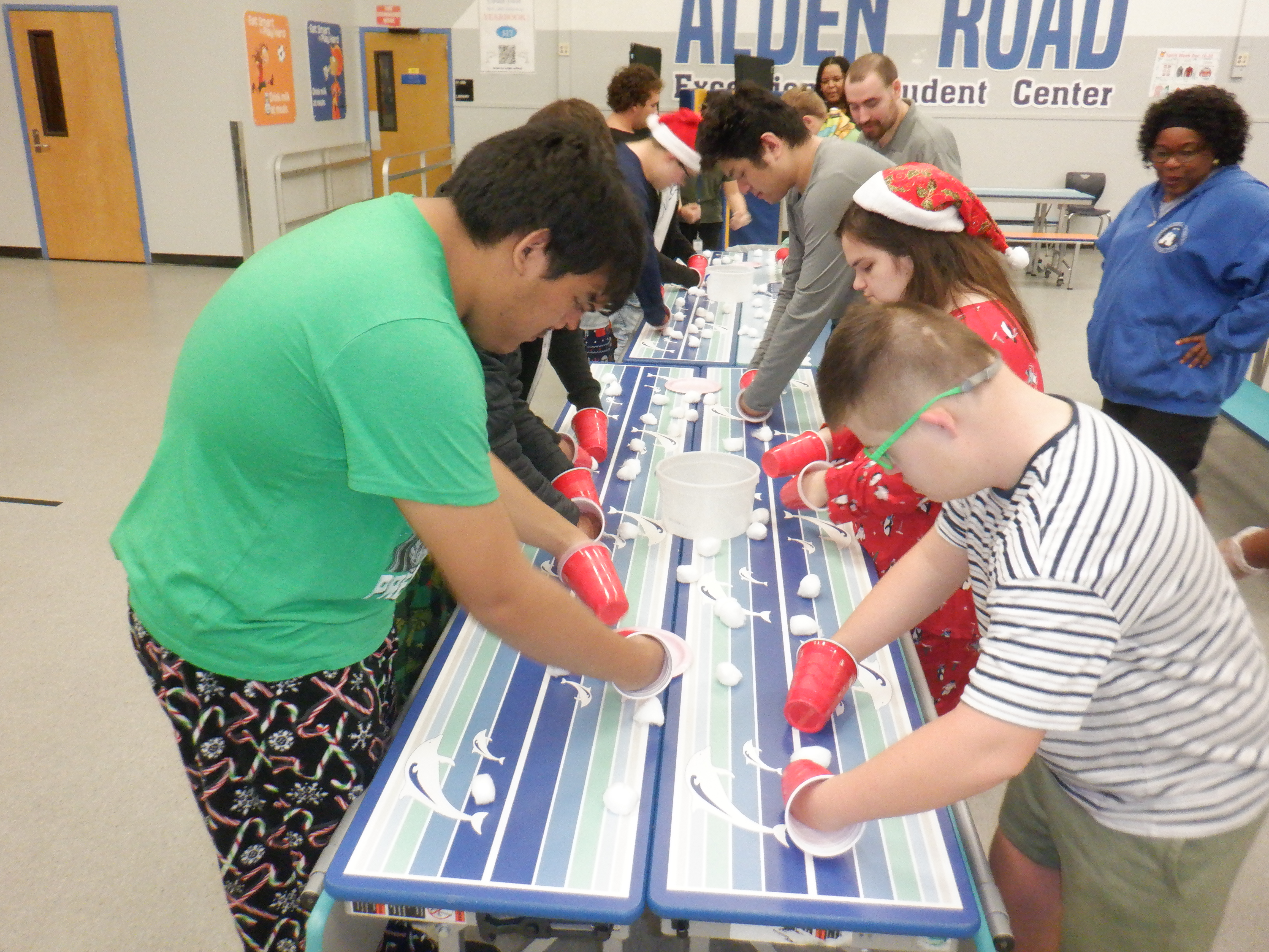 A group of people wearing winter clothing and glasses work on a blue table in a hallway.