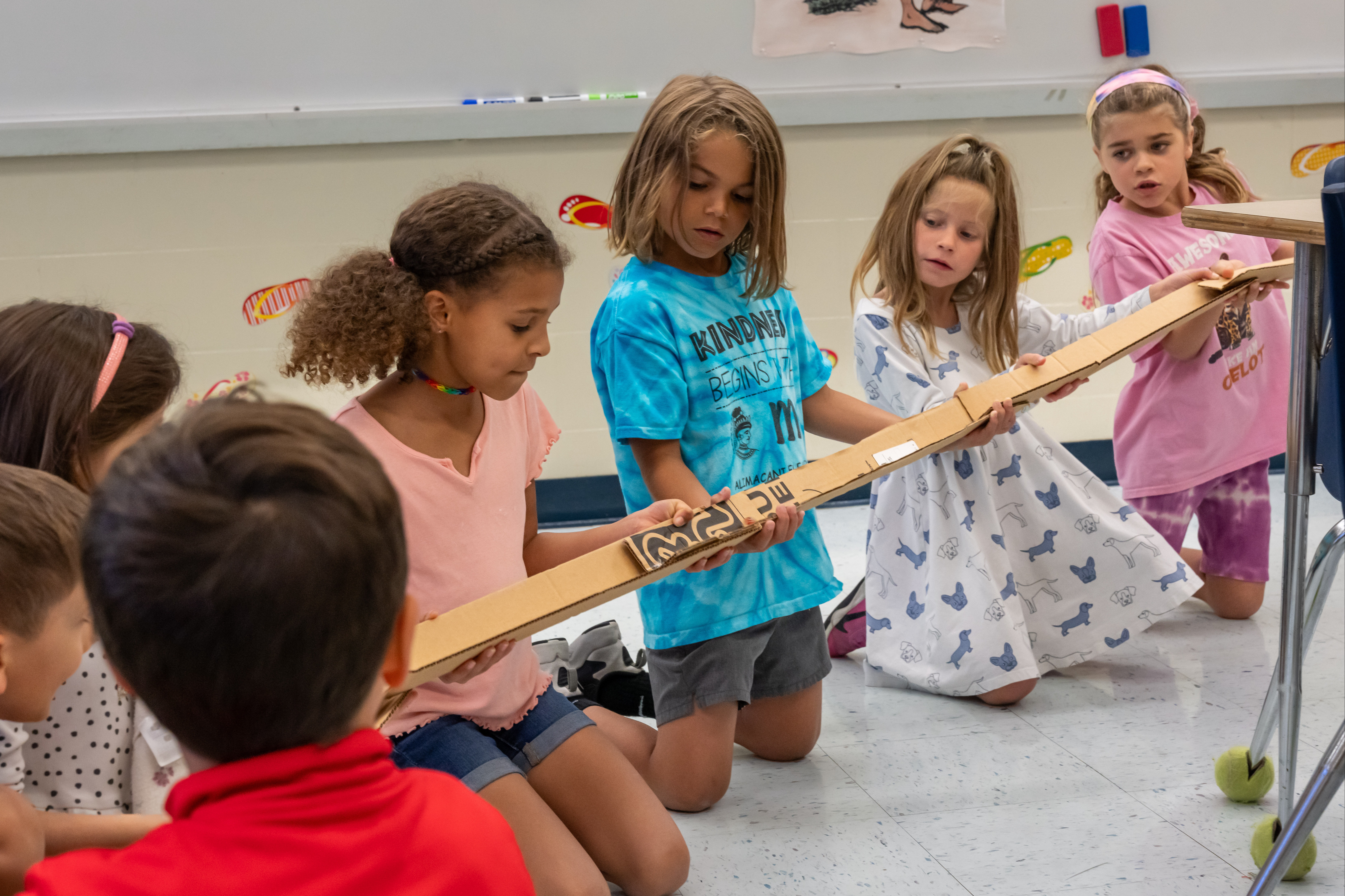 Students knelling on the floor working with a track made out of cardboard