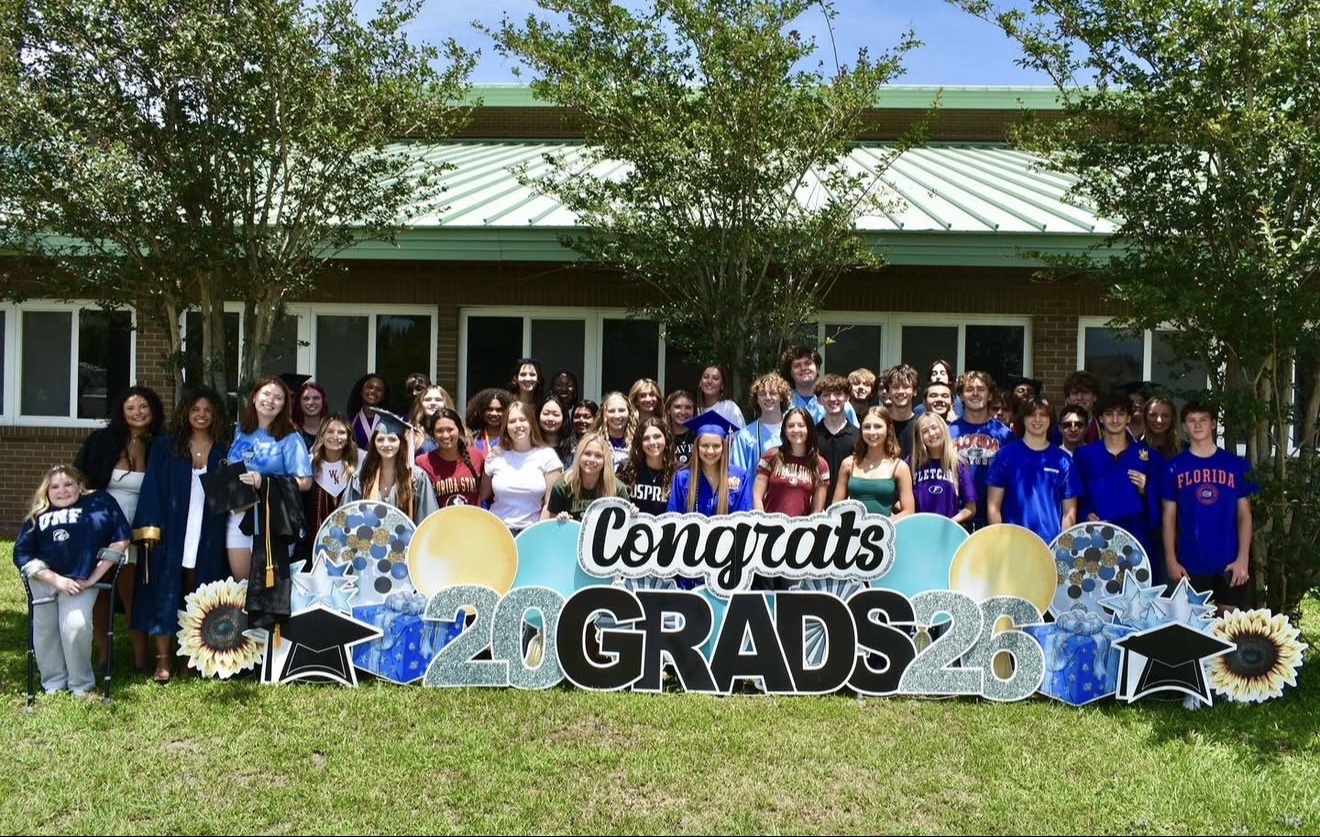 A large group of people in blue shirts pose for a picture in front of a building with "Congratulations 2023 Grads" sign.