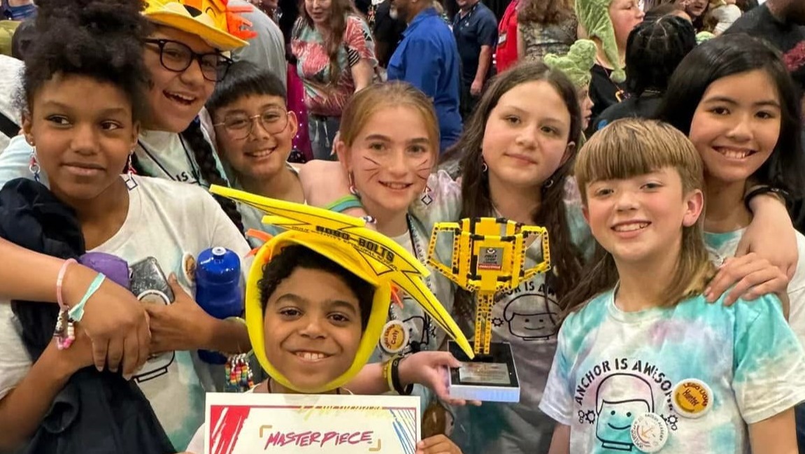 Group of children at a convention. One child holds a yellow crane trophy and a certificate.