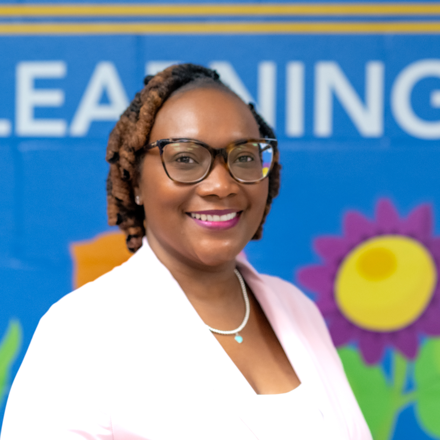Woman in glasses and pink blazer stands in front of blue backdrop with "LEARNING" text.