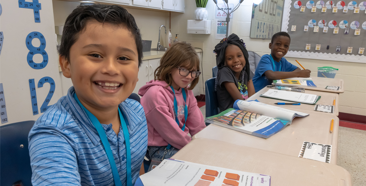 smiling students sitting at a table working on class assignments