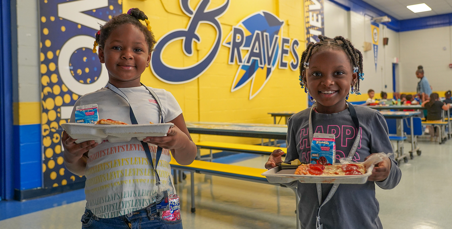 two students holding their lunch trays while smiling