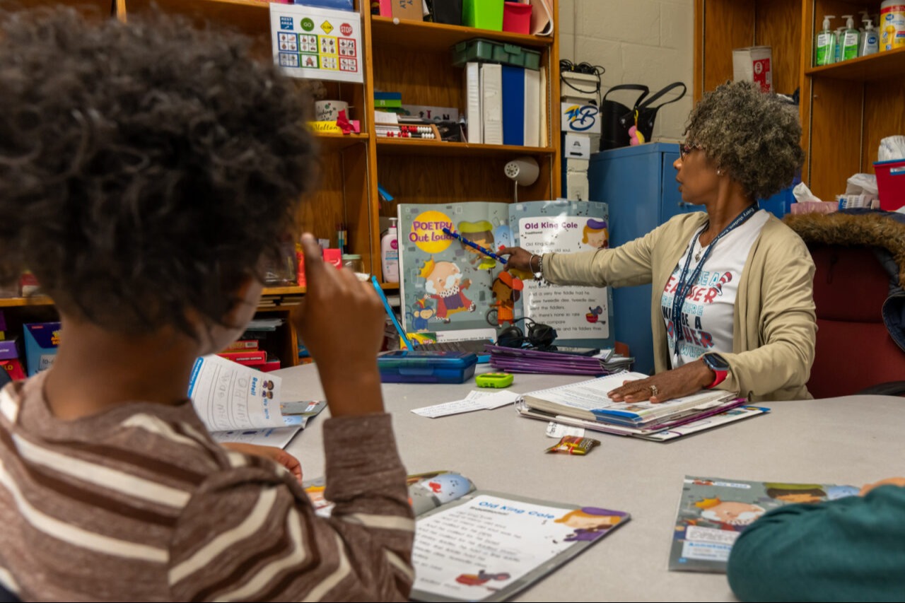 A teacher pointing to a book and reading to students
