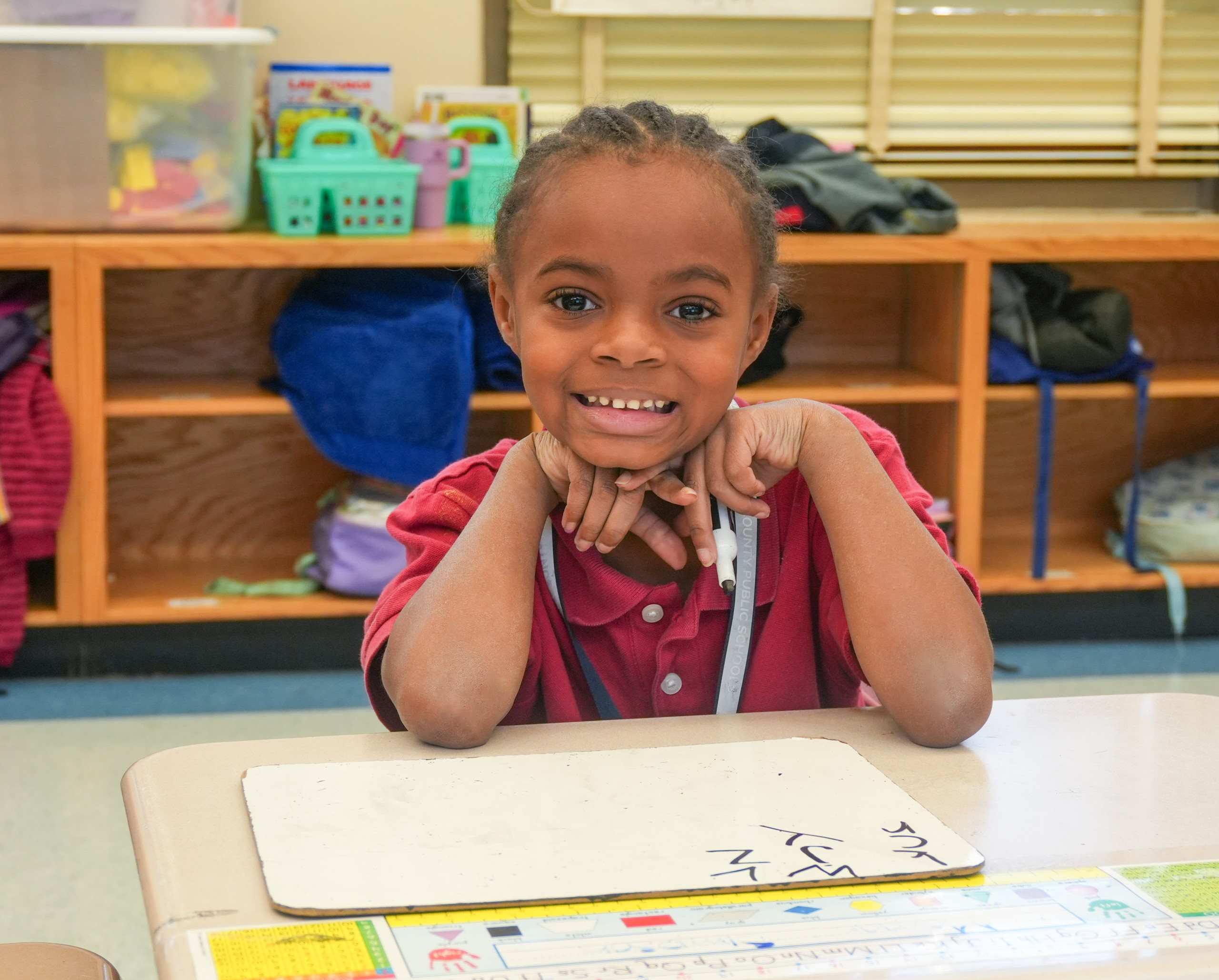 Student smiling at the camera with an expo marker in her hand and dry erase board at her desk