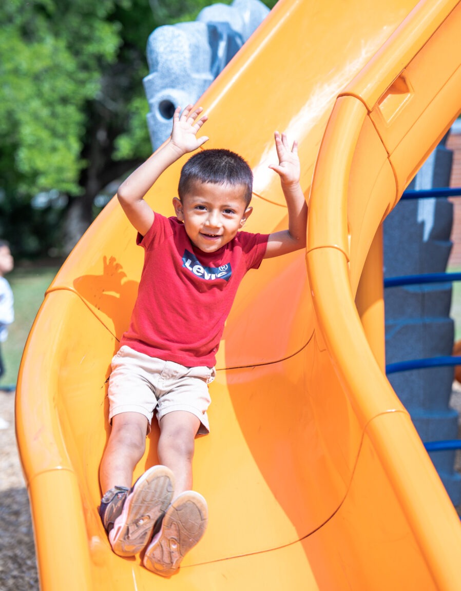 Student sliding down a slide with his hands up