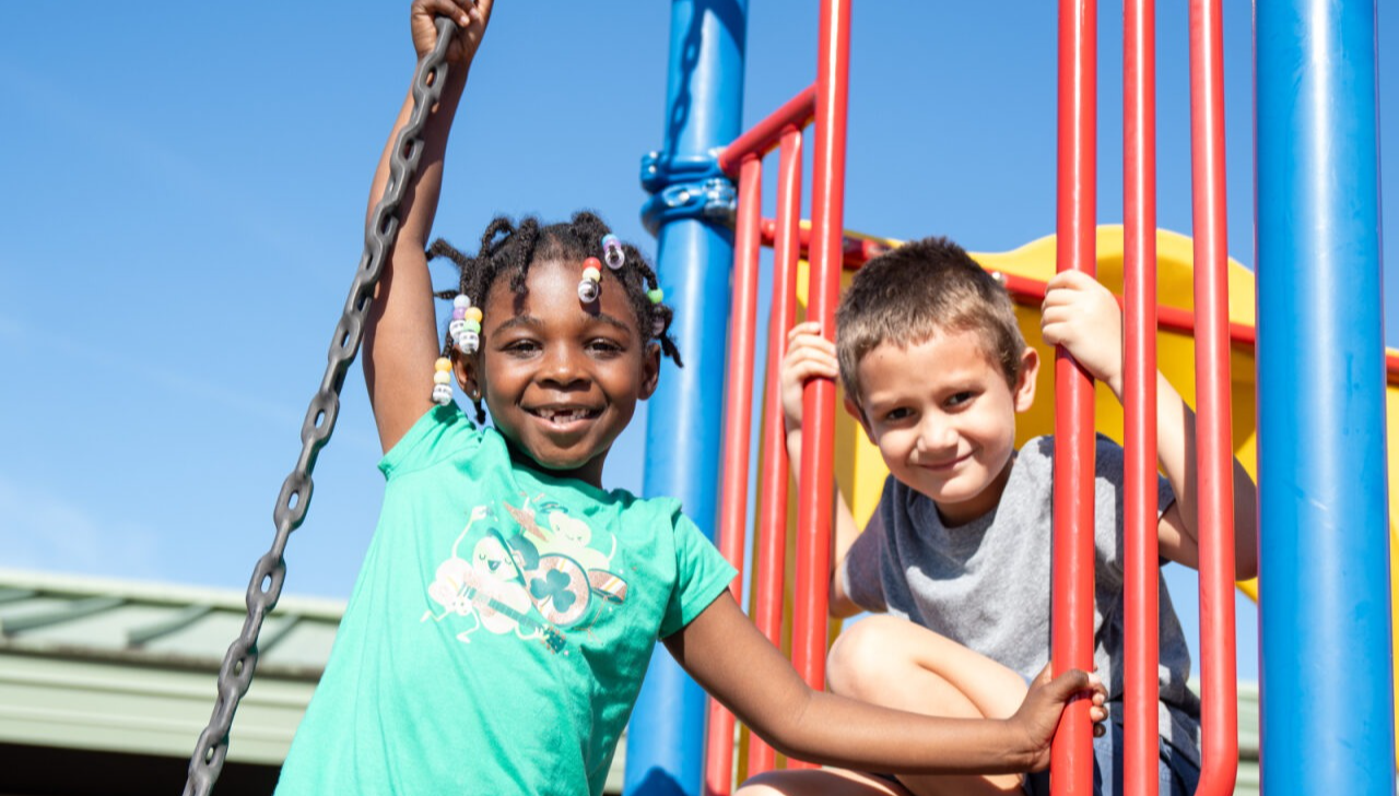 Two students smiling while climbing on the playground