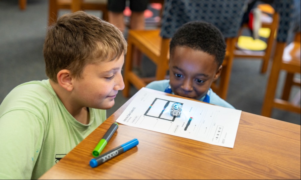 Two male students using color code for a small robot so it moves on its own along the path they coded.