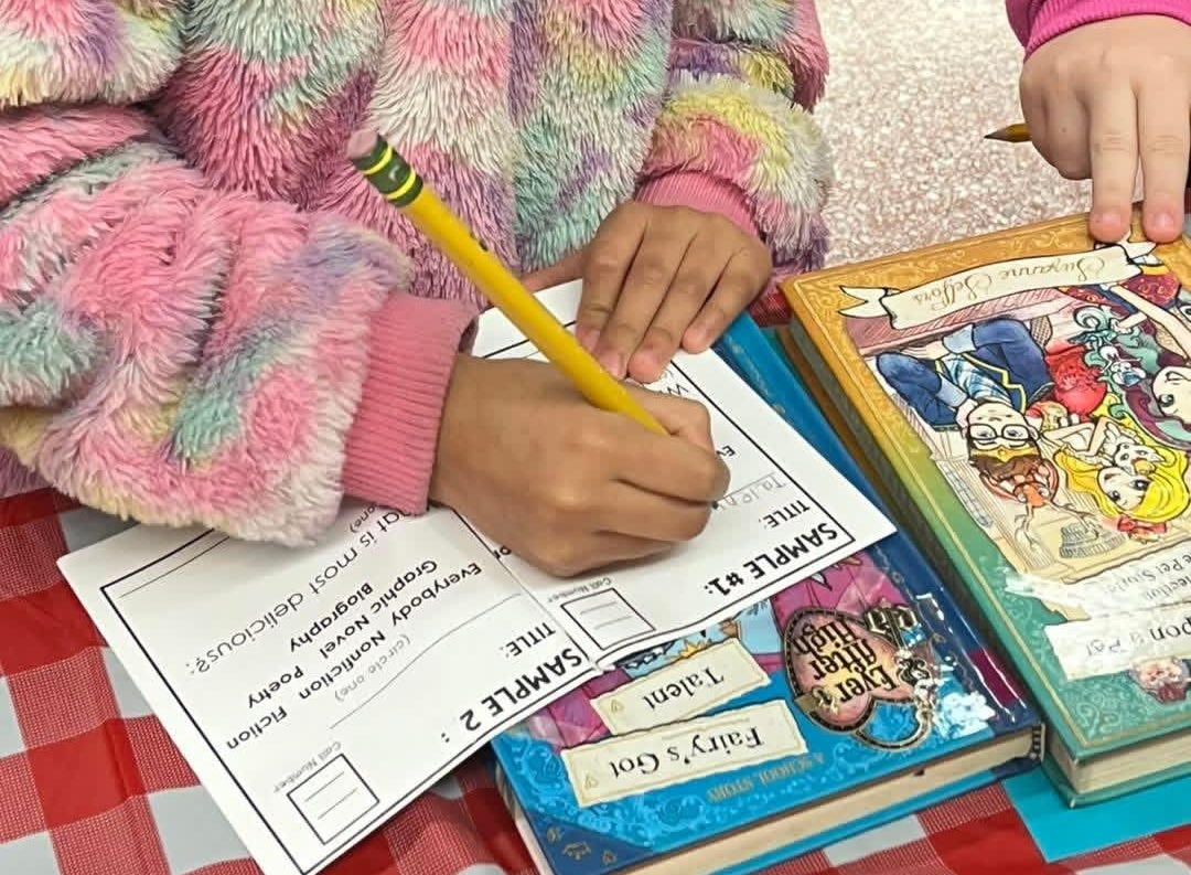 A young child sits at a table with a red tablecloth, using a pencil to write on a paper.