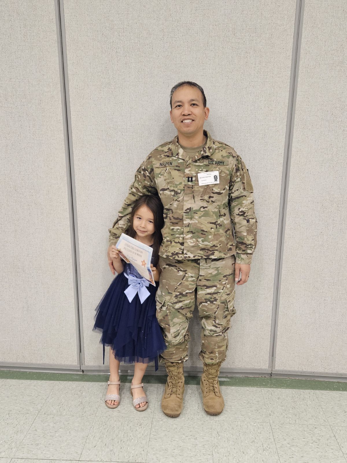 A military dad and his daughter holding an award.