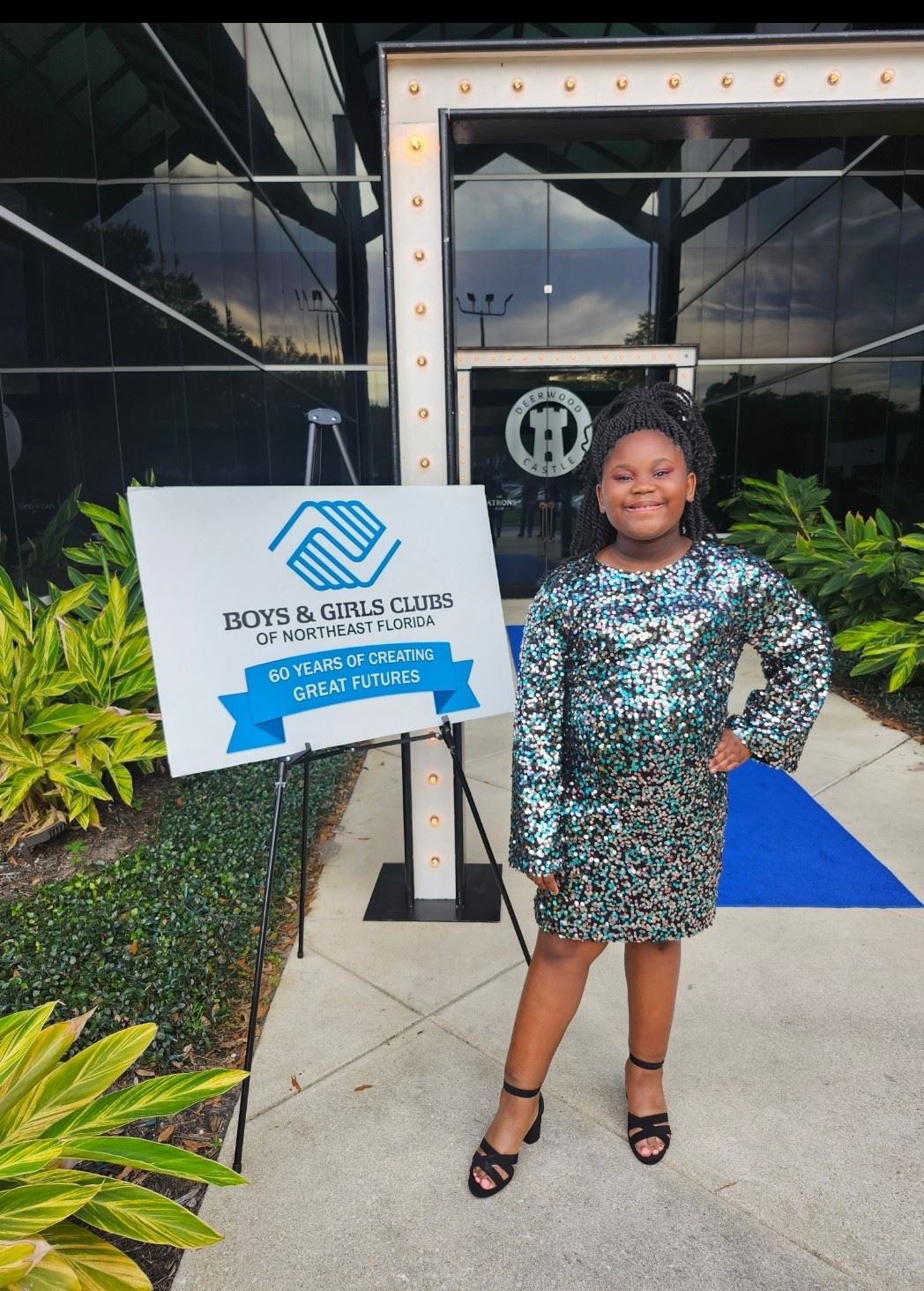 A person stands by a sign that reads "Boys & Girls Clubs of Northeast Florida" in front of a building.